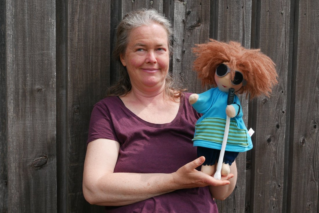 Handpuppe Willie mit Spielerein Anke Dübler vor einer grauen Holzfassade.