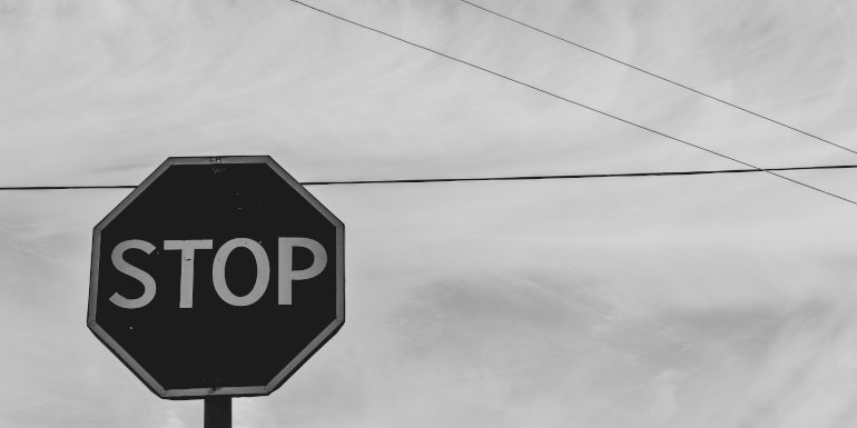 Schwarz-Weiß-Bild zeigt Stopschild vor einem Hintergrund aus Himmel und einzelnen Telefonleitungen
