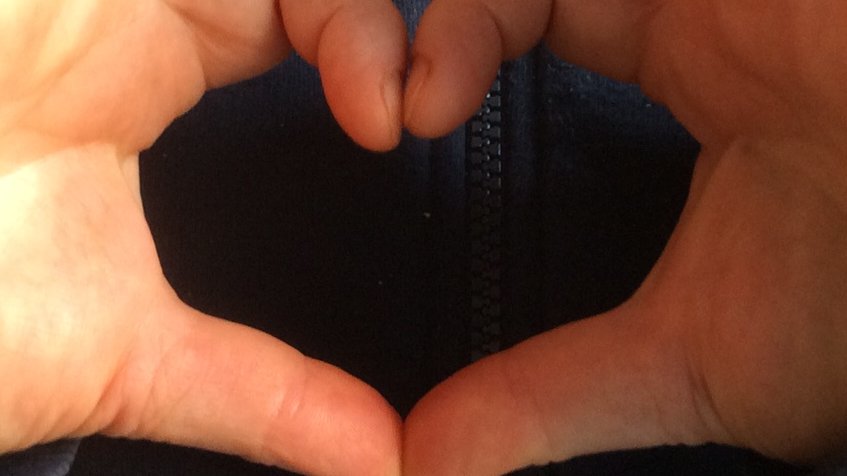 Zwei Hände formen ein Herz vor der Brust. 